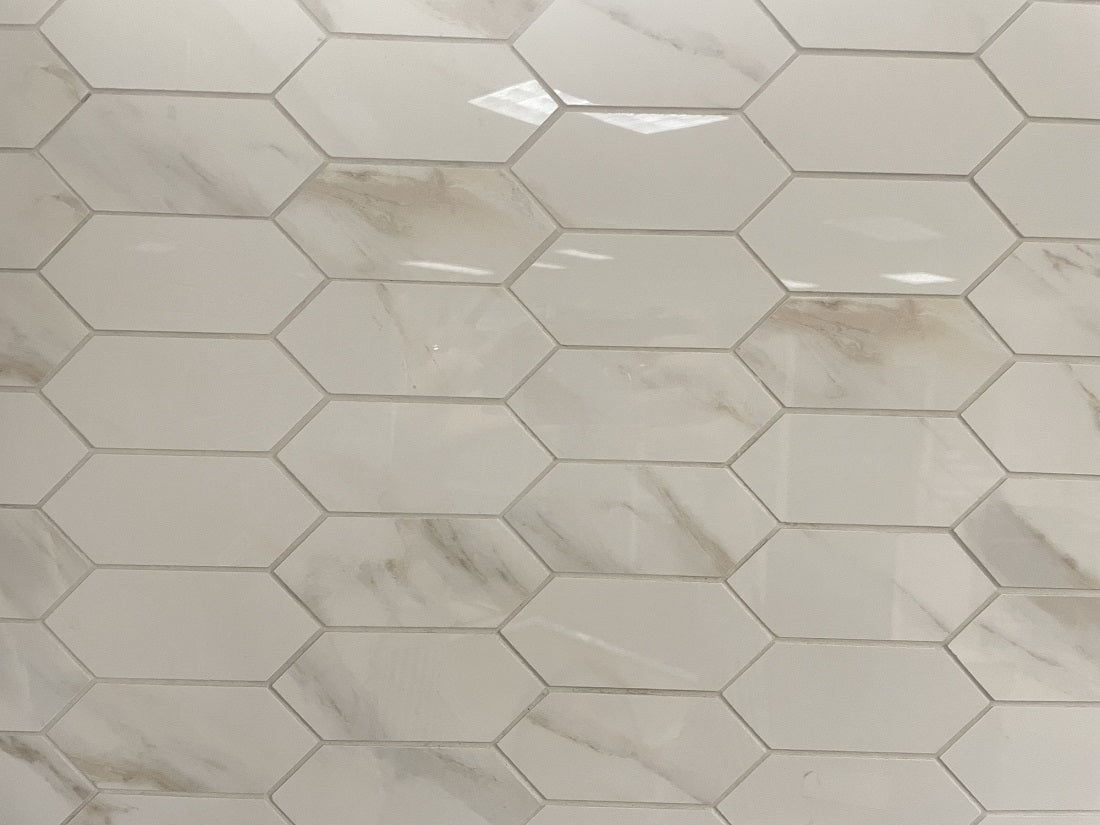 Calacatta Oro porcelain tile with a white/gold marble design, for floors and walls. In an elongated hexagon mosaic.