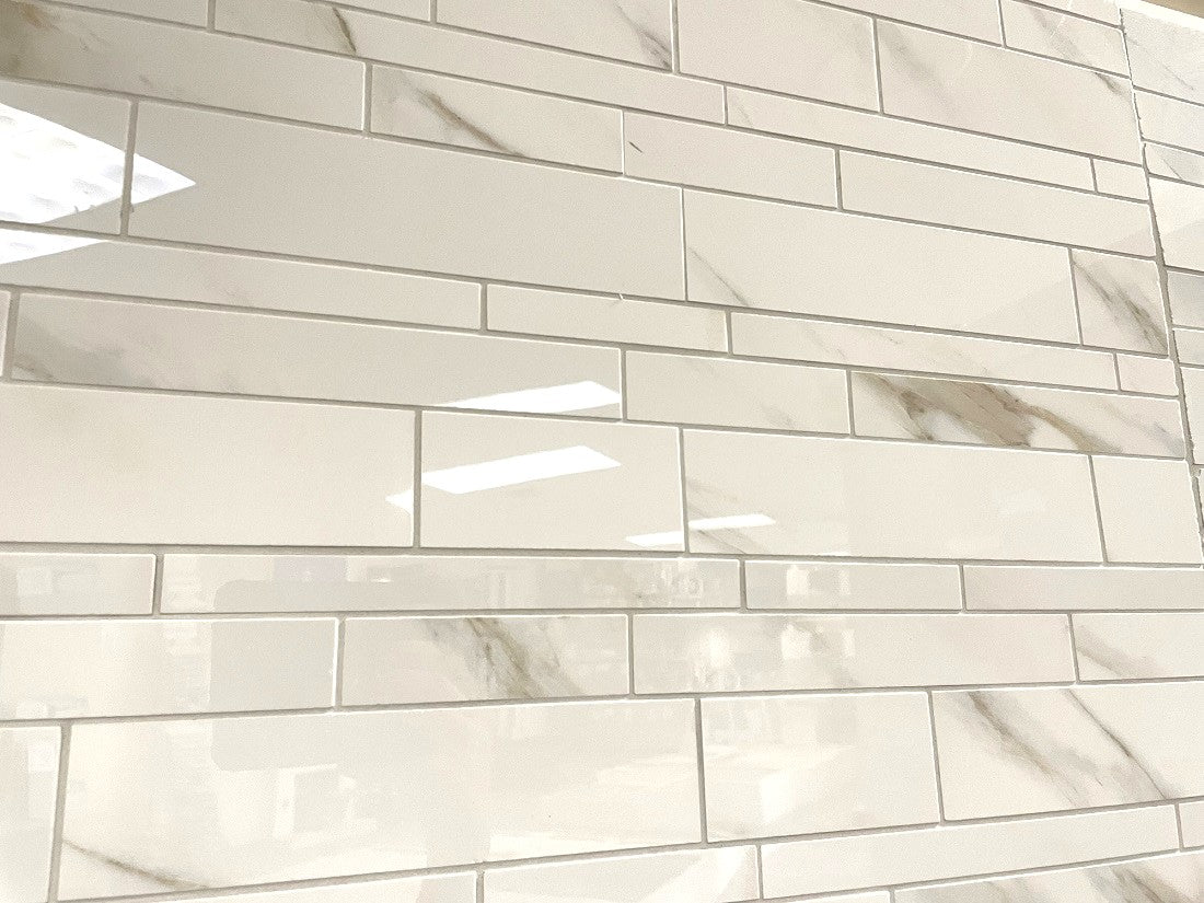 Calacatta Oro polished porcelain tile with a white/gold marble design, for floors and walls. In a random strip mosaic.