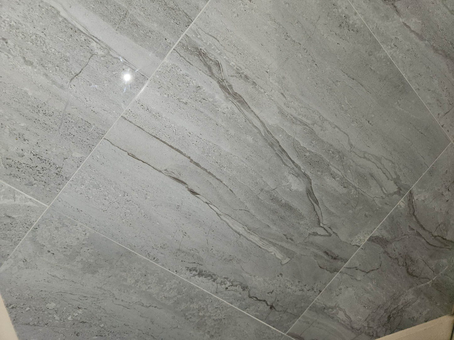 Vechia Cinza glossy ceramic tile with a grey travertine style, for floors and walls. In a 23x23" size.