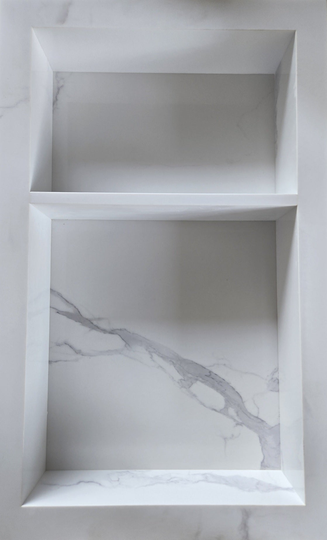 White Carrara prebuilt quartz shower niche made of engineered stone that offers shower storage, with a shelf.