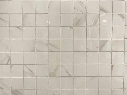 Calacatta Oro polished porcelain tile with a white/gold marble design, for floors and walls. In a 2x2" square mosaic.