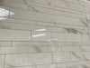 Calacatta Oro polished porcelain tile with a white/gold marble design, for floors and walls. In a random strip mosaic.