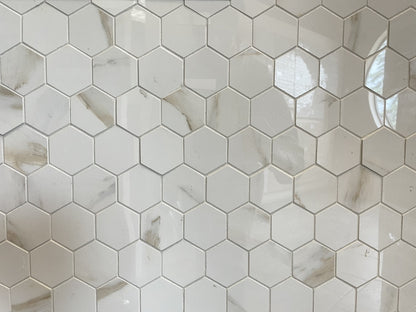 Calacatta Oro polished porcelain tile with a white/gold marble design, for floors and walls. In a small hexagon mosaic.