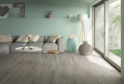 Corsica Argento matte ceramic tile with a grey wood design, for floors and walls. Made in Spain, installed in a room.